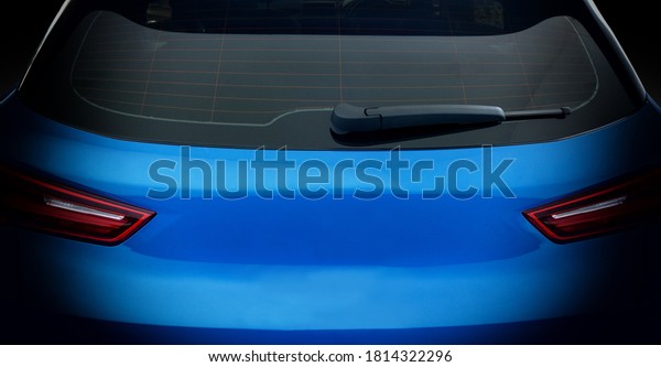 Rear view of blue car with rear\
wiper, defogger wires and rear lights on dark tone\
background.