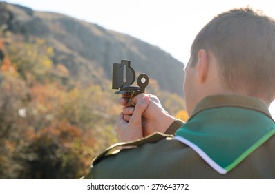 Rear View Of A Boy Scout Navigating In The Wilderness While Taking A Reading On A Mountain With His Magnetic Compass Device