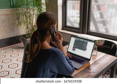 Rear View Of Brunette Business Woman Working On Computer And Speaking On Phone. Caucasian Female Working Online, Internet Shopping, Checking Social Network. Home Office, Flexible Way Of Work Concept.