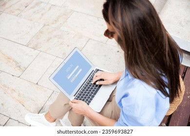 Rear view of a brunette haired woman sitting outdside and using laptop. Unrecognizable female loging in to the internet bank.