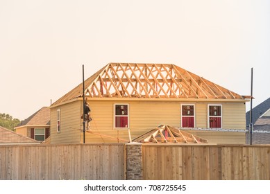 Rear View Of Builder At Stick Built Wooden House Construction Site Near Completed Suburban Home In Humble, Texas, US During Sunset. Framing Contractor Wears Tool Belt On Scaffolding. Labor Day Concept