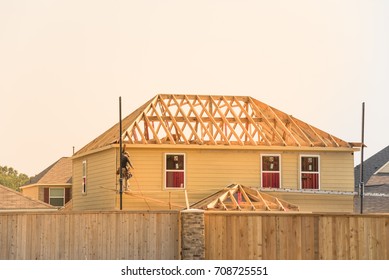 Rear View Of Builder At Stick Built Wooden House Construction Site Near Completed Suburban Home In Humble, Texas, US During Sunset. Framing Contractor Wears Tool Belt On Scaffolding. Labor Day Concept