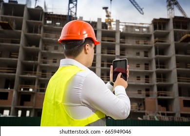 Rear view of building inspector holding digital tablet and inspecting building under construction