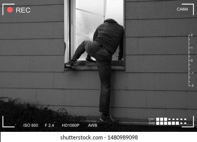 Rear View Of A Burglar Entering In A House Through A Open Window