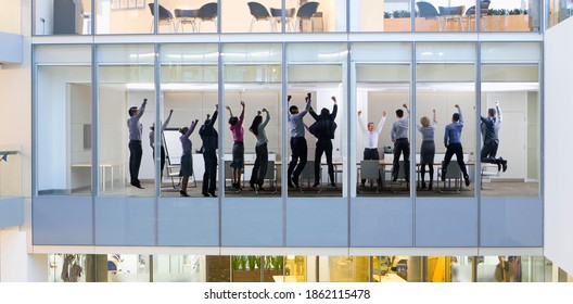 A rear view of business people celebrating their success in a conference room seen through the glass walls from outside of a modern building - Powered by Shutterstock