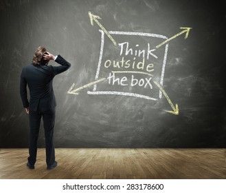 Rear View Of Business Person Scratching Head With Hand In Confusion Standing In Front Of Chalkboard With Drawing Illustrating Creative Thinking - Think Outside The Box Concept