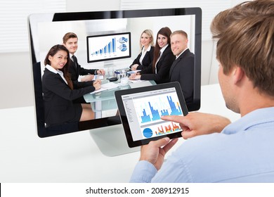 Rear view of businessman analyzing graphs on computer while video conferencing in office - Powered by Shutterstock