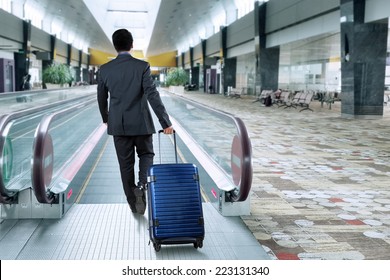 Rear view of businessman carrying luggage walk toward escalator in airport hall - Powered by Shutterstock