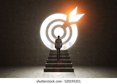 Rear view of a businessman climbing stairs. Large target on the wall is glowing with orange light. Toned image - Shutterstock ID 520195351