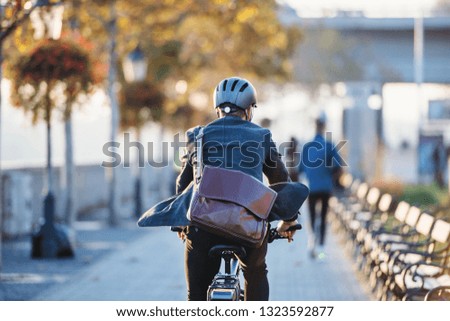 A rear view of businessman commuter with electric bicycle traveling to work in city.