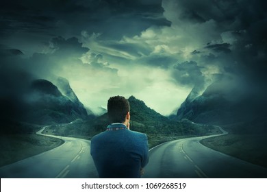 Rear View Of A Businessman In Front Of A Crossroad, Fork Junction Where A Road Is Splitted In Two Different Ways. Choosing The Correct Way Between Left And Right, Failure Or Success.Difficult Decision