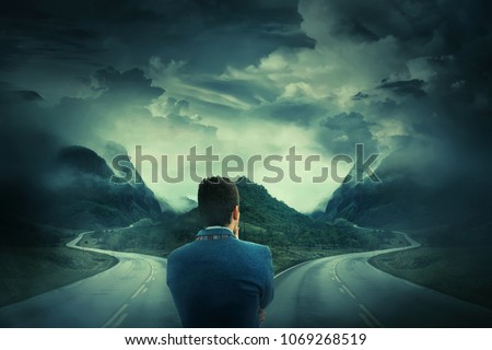 Rear view of a businessman in front of a crossroad, fork junction where a road is splitted in two different ways. Choosing the correct way between left and right, failure or success.Difficult decision