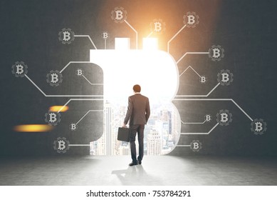 Rear view of a businessman holding a suitcase and looking at a cityscape standing in a dark room with bitcoin network sketch and a large bitcoin sign opening in the wall. Toned image mock up - Powered by Shutterstock