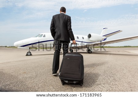 Rear view of businessman with luggage walking towards corporate jet