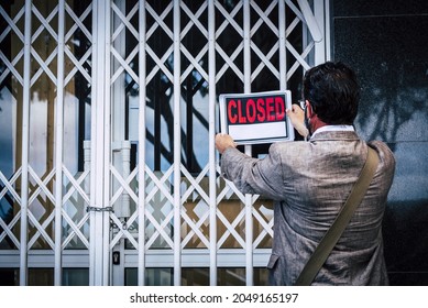 Rear view of businessman putting closed sign on display on locked shop or office due to outbreak of coronavirus pandemic. Government shutdown of non essential services. Closing due to bankruptcy