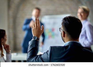 Rear view of a businessman raising his hand to ask the question during business presentation in the office.