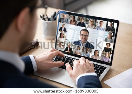 Rear view of businessman speak on web conference with diverse colleagues using laptop Webcam, male employee talk on video call with multiracial coworkers have online meeting briefing from home