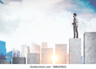 Rear view of a businessman standing on a giant bar chart and looking at a city panorama in front of him. Toned image. Mock up - Shutterstock ID 588659822