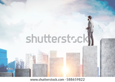 Rear view of a businessman standing on a giant bar chart and looking at a city panorama in front of him. Toned image. Mock up