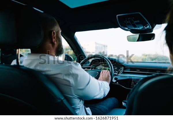 Rear view of businessman steering luxury\
expensive car for getting to trip destination, male driver enjoying\
automotive wheeling in motorized modern vehicle, concept of\
executive transportation