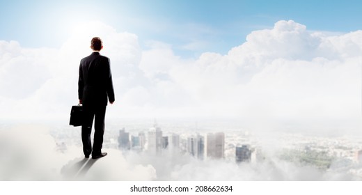 Rear view of businessman with suitcase standing on cloud - Powered by Shutterstock