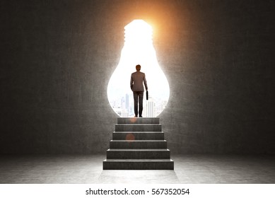 Rear view of a businessman with a suitcase standing on a stairs near a light bulb shaped opening in a black wall. Toned image. - Shutterstock ID 567352054