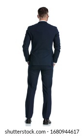 rear view of a businessman wearing navy suit standing with hands in pocket and looking ahead on white studio background
