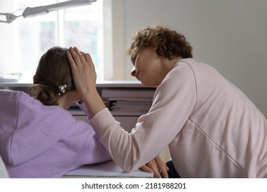 Rear View Caring Mother Comforting Upset Depressed Teenage Daughter, Touching Head, Expressing Empathy And Love, Young Mum Supporting Tired Sad Teen Schoolgirl Sitting At Desk At Home