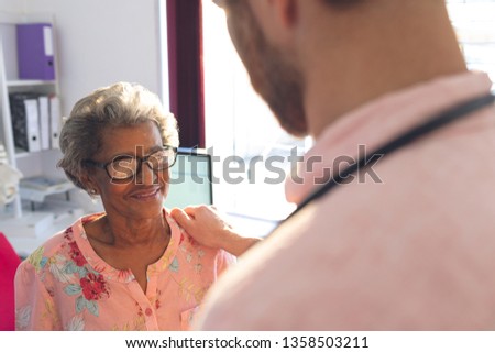 Rear view of a Caucasian confident male doctor interacting with female senior patient in clinic