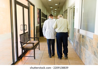 Rear View Of A Caucasian Doctor And Elderly Mature Retired Man Walking Together At The Retirement Home