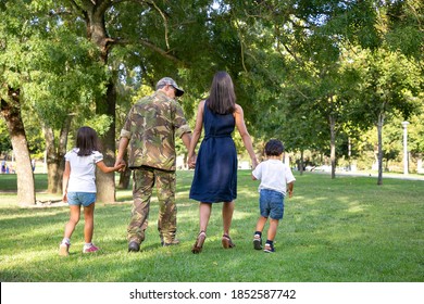 Rear view of Caucasian family holding hands and walking together in city park. Dad in camouflage uniform, long-haired mom and children enjoying holiday on nature. Family reunion and weekend concept - Shutterstock ID 1852587742