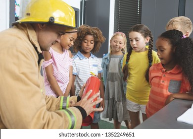 Rear view of a Caucasian firefighter wearing a fire helmet over his head and teaching about fire extinguisher to school kids in classroom at school - Powered by Shutterstock