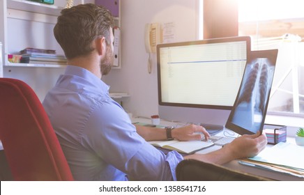 Rear View Of Caucasian Male Doctor Checking  X Ray Report In Computer At Clinic 