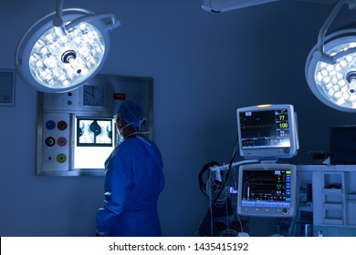 Rear view of Caucasian male surgeon reading x ray in operating room at hospital - Powered by Shutterstock