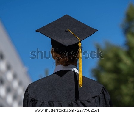 Rear view of caucasian woman in graduate gown near university. 