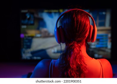 Rear view of a caucasian woman playing a computer game in neon light in the dark. - Powered by Shutterstock