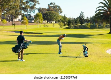 Rear View Of Caucasian Young Man Standing With Golf Bag While African American Friend Playing Golf. Summer, Unaltered, Friendship, Togetherness, Nature, Sport And Weekend Activities Concept.