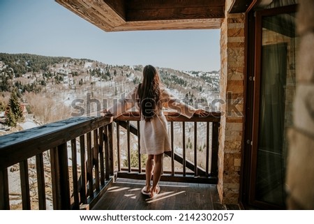 Rear view of charming young woman in bathrobe enjoying the winter nature on the large terrace