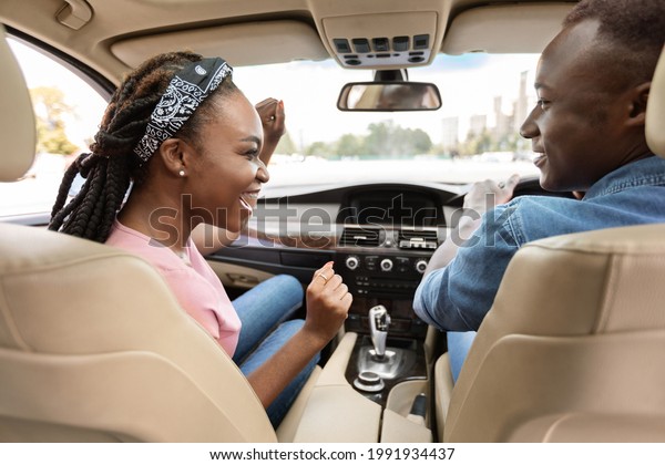 Rear view of\
cheerful african american couple sitting in nice car, going\
vacation together by car. Emotional black millennial man and woman\
enjoying trip, having conversation,\
laughing