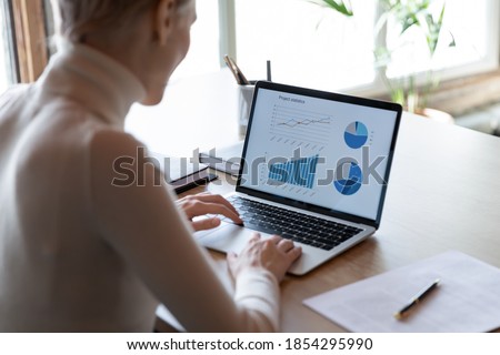Rear view close up businesswoman working with financial project statistics on laptop, accountant employee analyzing data, graphs charts, report, looking at computer screen, sitting at work desk