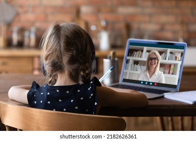 Rear view close up little girl wearing headphones watching webinar at home, using laptop, studying online, writing notes, student listening to older woman mentor teacher, homeschooling concept - Powered by Shutterstock