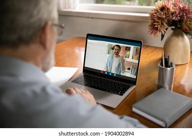 Rear View Close Up Senior Man Watching Webinar, Learning Language Online, Sitting At Desk, Young Teacher Mentor Teaching Mature Student, Explaining Presenting Information, Making Video Call