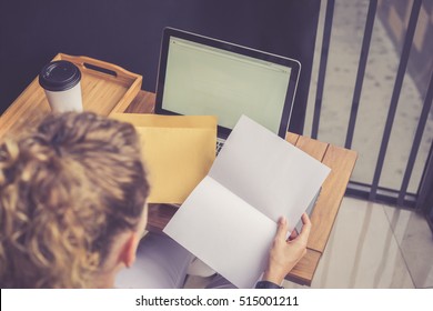 Rear View Close-up Letter And Gold Envelope In Girl's Hands. Girl Sitting At Wooden Table On Which Is Laptop,next To Cup Of Coffee. Woman Reading Open Letter. Gift Certificate. Congratulation.