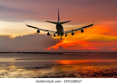 Rear View Commercial Passenger Aircraft Or Cargo Transportation Airplane Fly Over Coast Of Sea After Takeoff From Airport In Evening With Red Sky