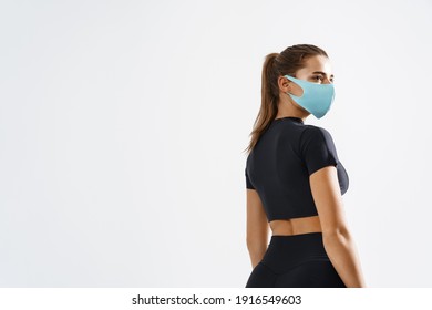 Rear View Of Confident Fitness Woman Looking Aside In Protective Face Mask. Sporty Female Athlete With Fit Body, Turn Head And Look Away, Workout Indoors, White Background.