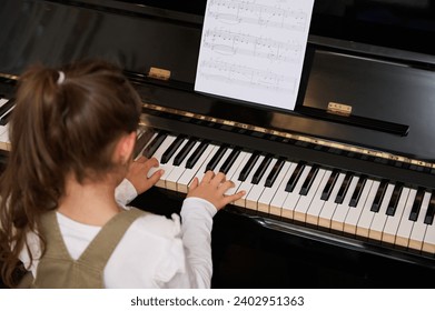 Rear view confident talented little child girl 6-8 years old, learning music, performing the rhythm of classical music while playing grand piano, putting fingers on keys and enjoying classical music - Powered by Shutterstock