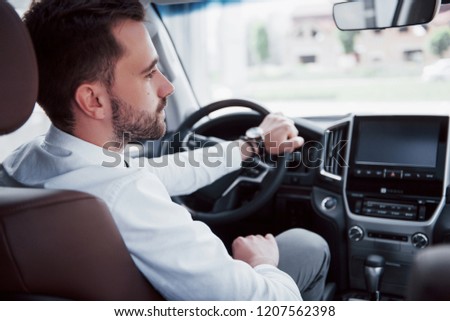 Rear view of confident young businessman sitting at the wheel of his new car.