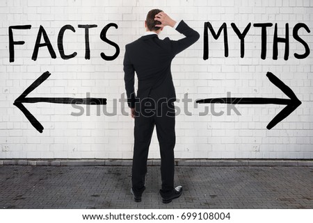 Rear view of confused businessman looking at arrow signs below facts and myths text