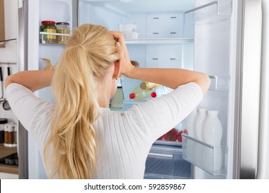 Rear View Of A Confused Woman Looking Inside The Fridge