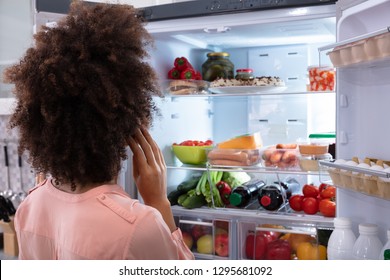 Rear View Of A Confused Woman Searching For Food In An Open Refrigerator - Powered by Shutterstock